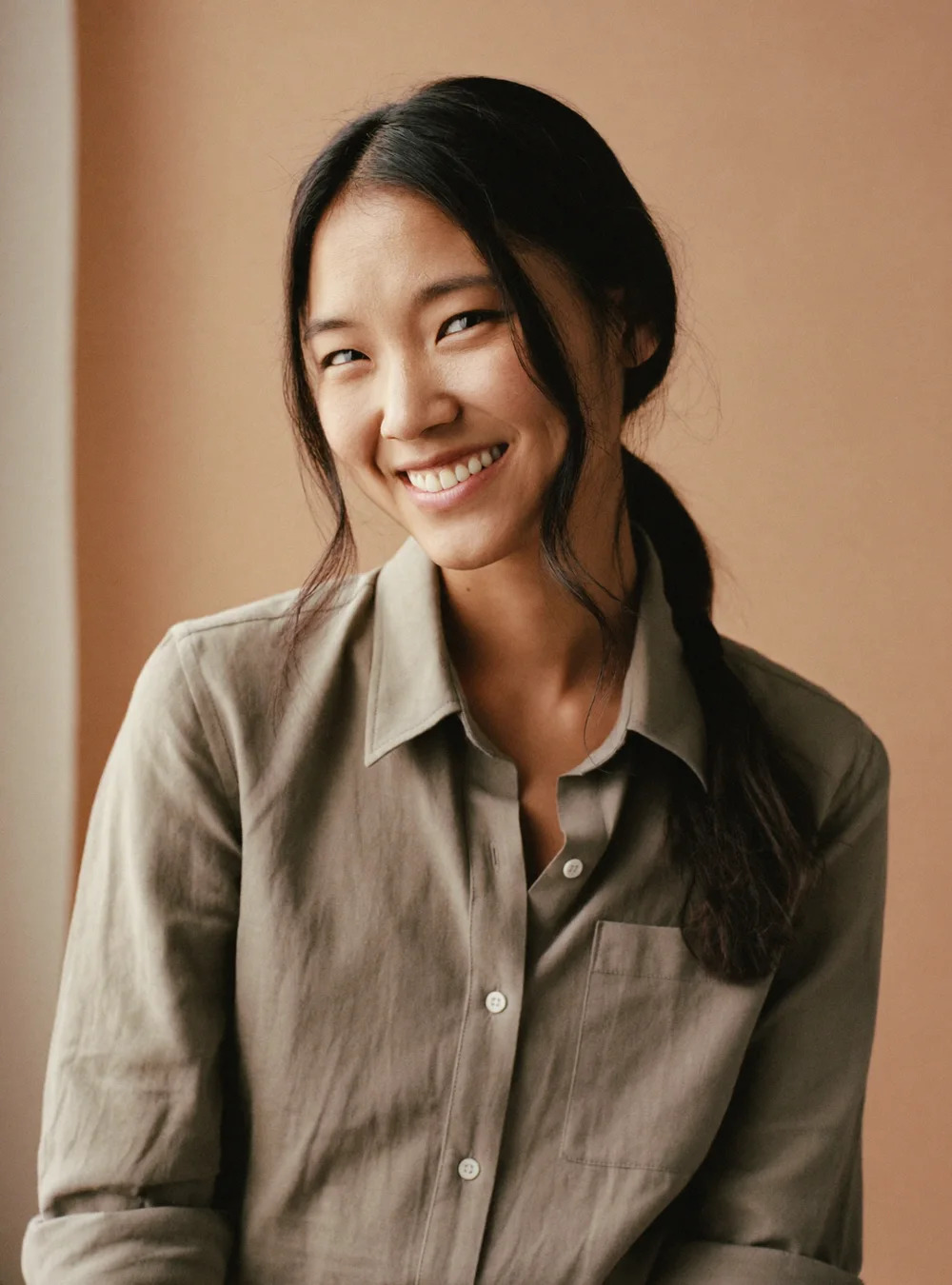 Portrait of Maya Chen in a sage linen shirt, smiling brightly